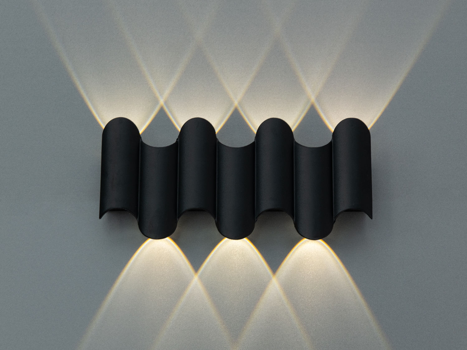 Хвилястий настінний світильник з чорного металу, який випромінює світло у формі перехресних променів на стіні.