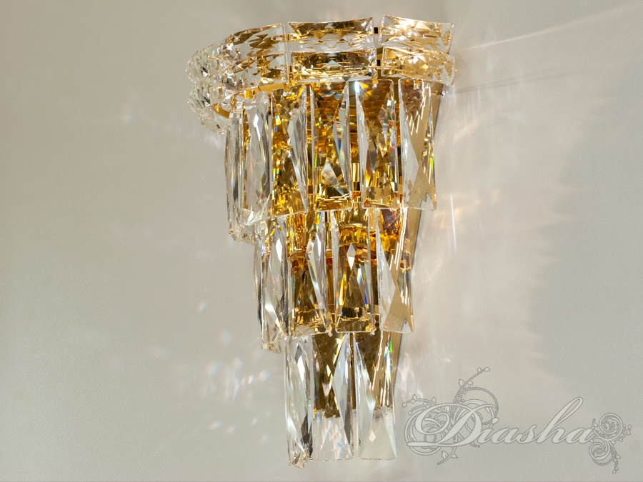 Конструкція світильника включає в себе сміливе поєднання металу та скла, де матові та поліровані металеві елементи створюють контраст з прозорими кришталевими стрижнями, що падають каскадом.