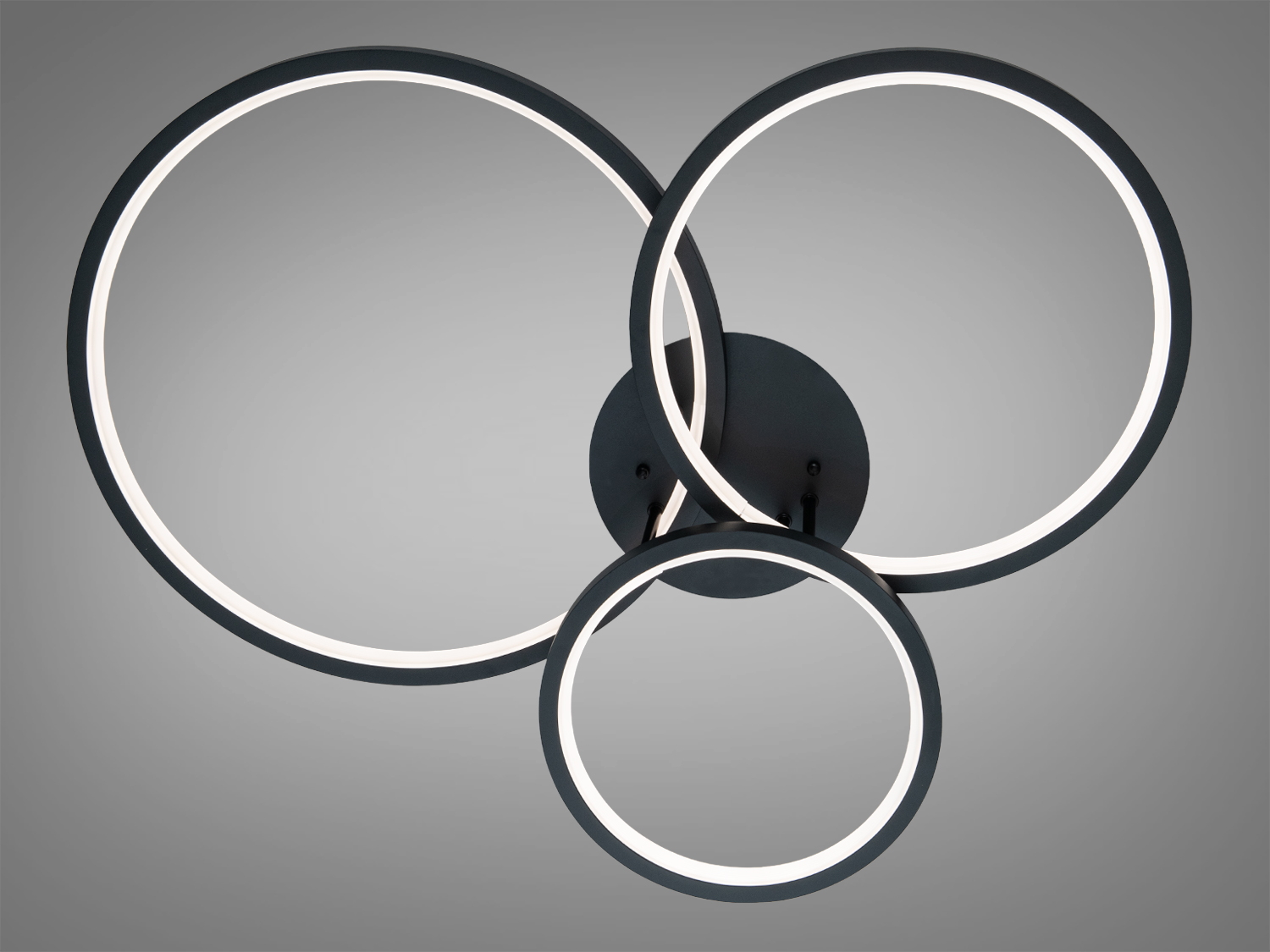 Люстра з трьома чорними кільцями, встановлена на стелі, забезпечує рівномірне освітлення завдяки своєму мінімалістичному дизайну.