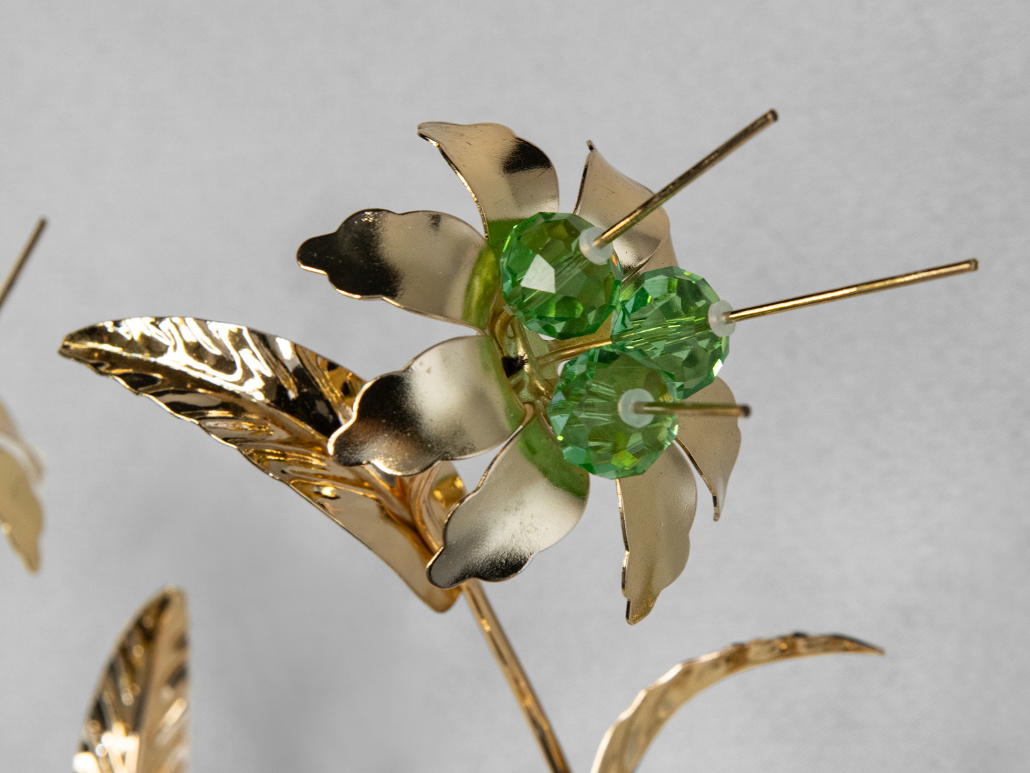 Крупний план металевої квітки з зеленими кристалами, що підкреслює деталі та текстуру матеріалу.