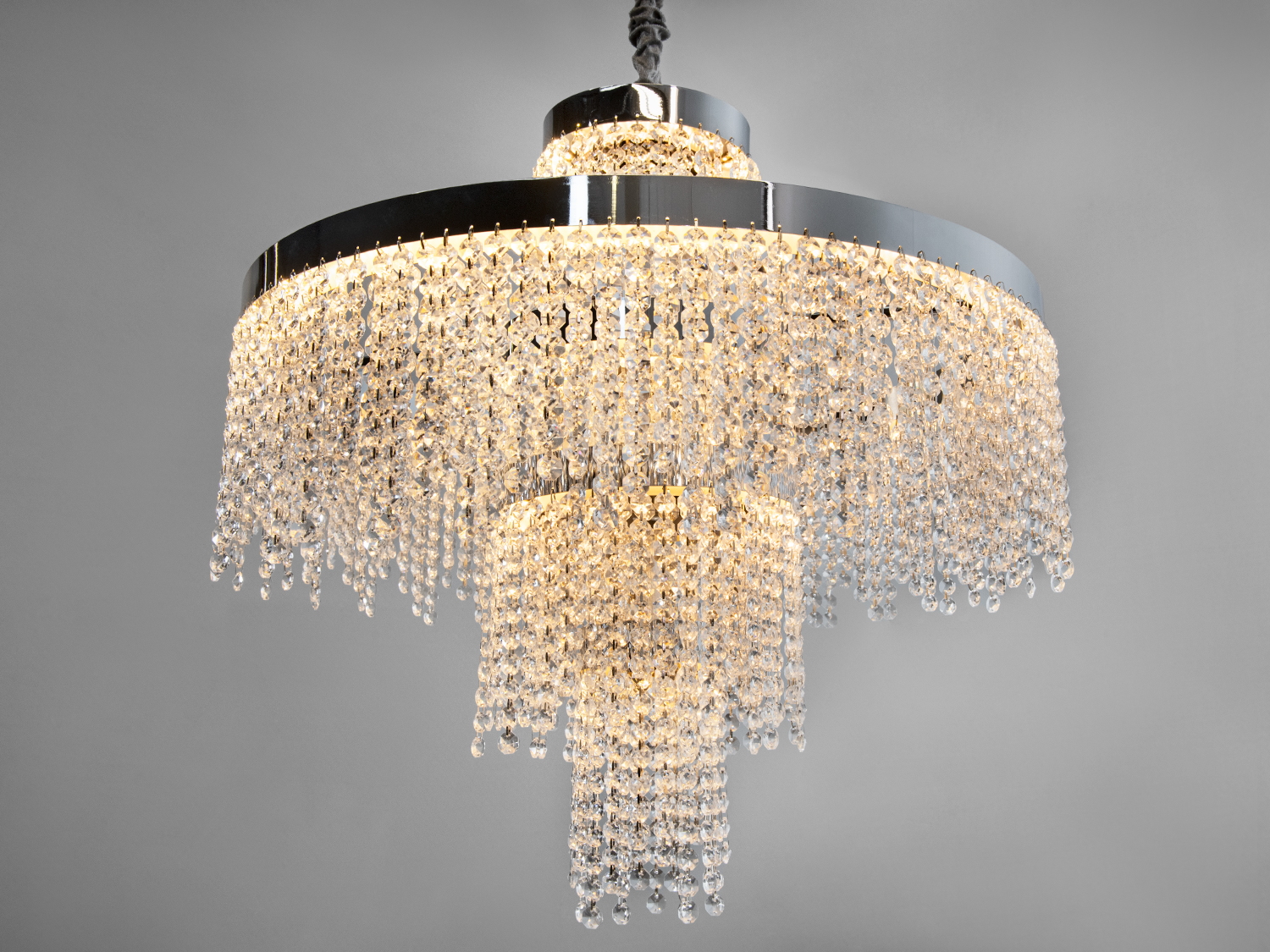 Кришталева люстра з каскадним дизайном, що підвішується до стелі. Вона створює тепле освітлення, підходить для вітальні або їдальні.