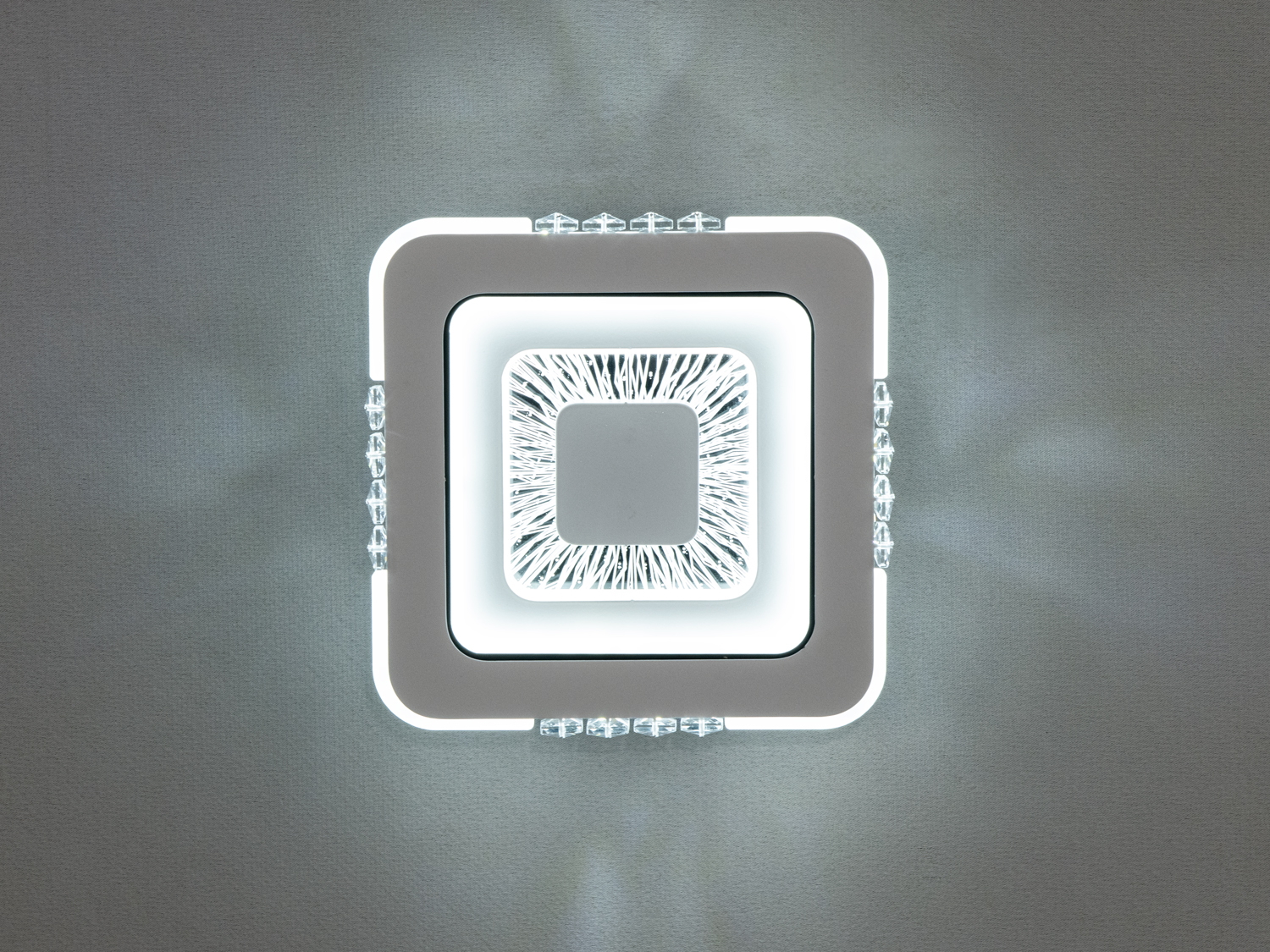 Білий квадратний світильник має чітку квадратну форму, доповнену плавними лініями, які мяко окреслюють контур.