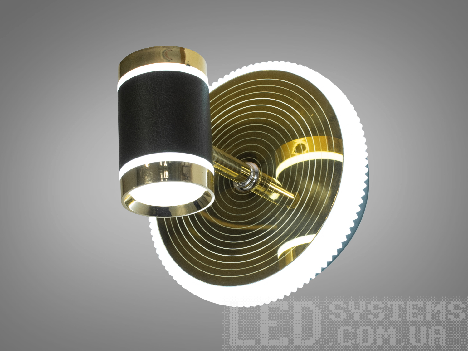 Світильник з круглою основою, що має концентричні золоті кільця, та циліндричний абажур з чорної шкіри, створює стильний акцент.