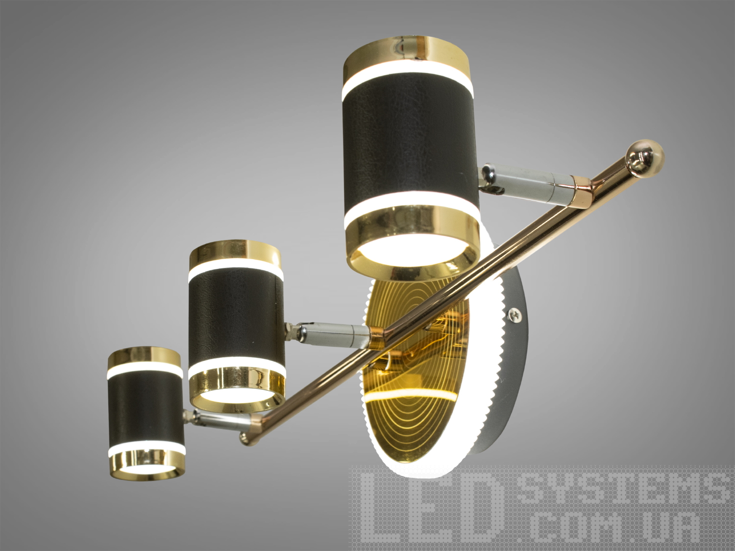 Світильник з трьома циліндричними лампами, чорний з золотистими деталями, монтується на стіну, ідеальний для освітлення вітальні.