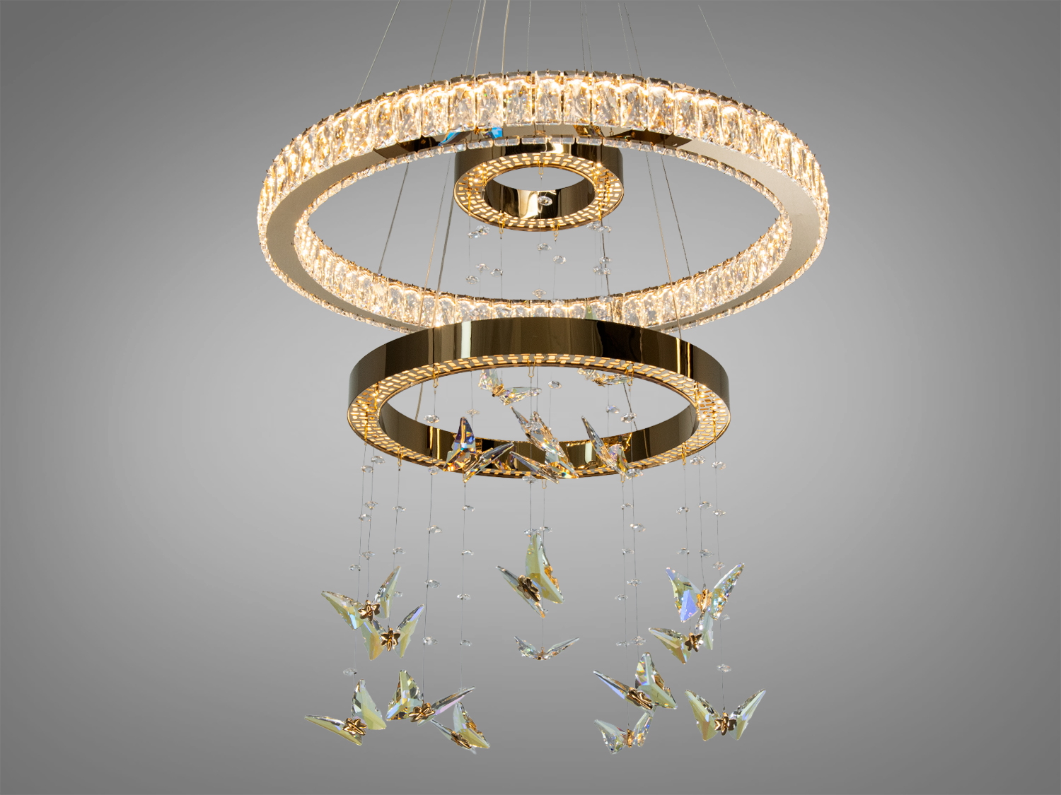 Люстра з трьома кільцями, прикрашена кришталевими метеликами, підвішена на тонких дротах для створення ефекту легкості в інтер′єрі.