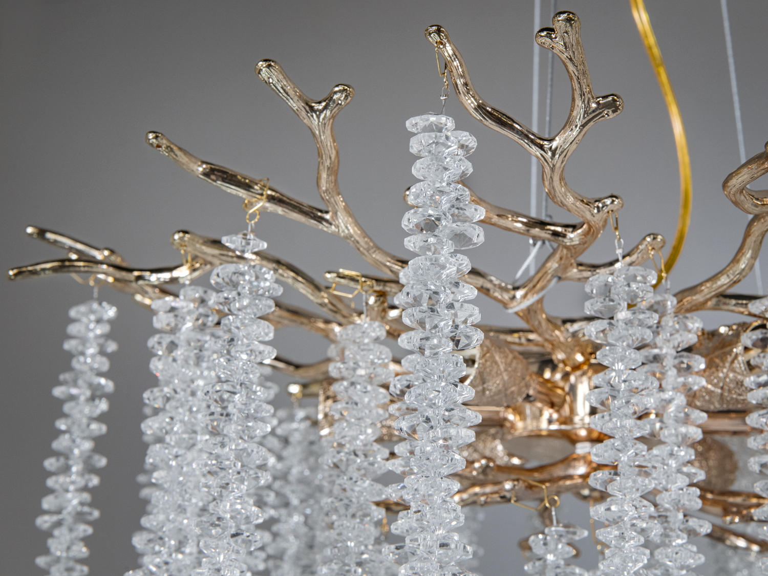 Деталь люстри з кришталевими підвісками, що висять з гіллястої основи, додає елегантності та блиску будь-якому простору.
