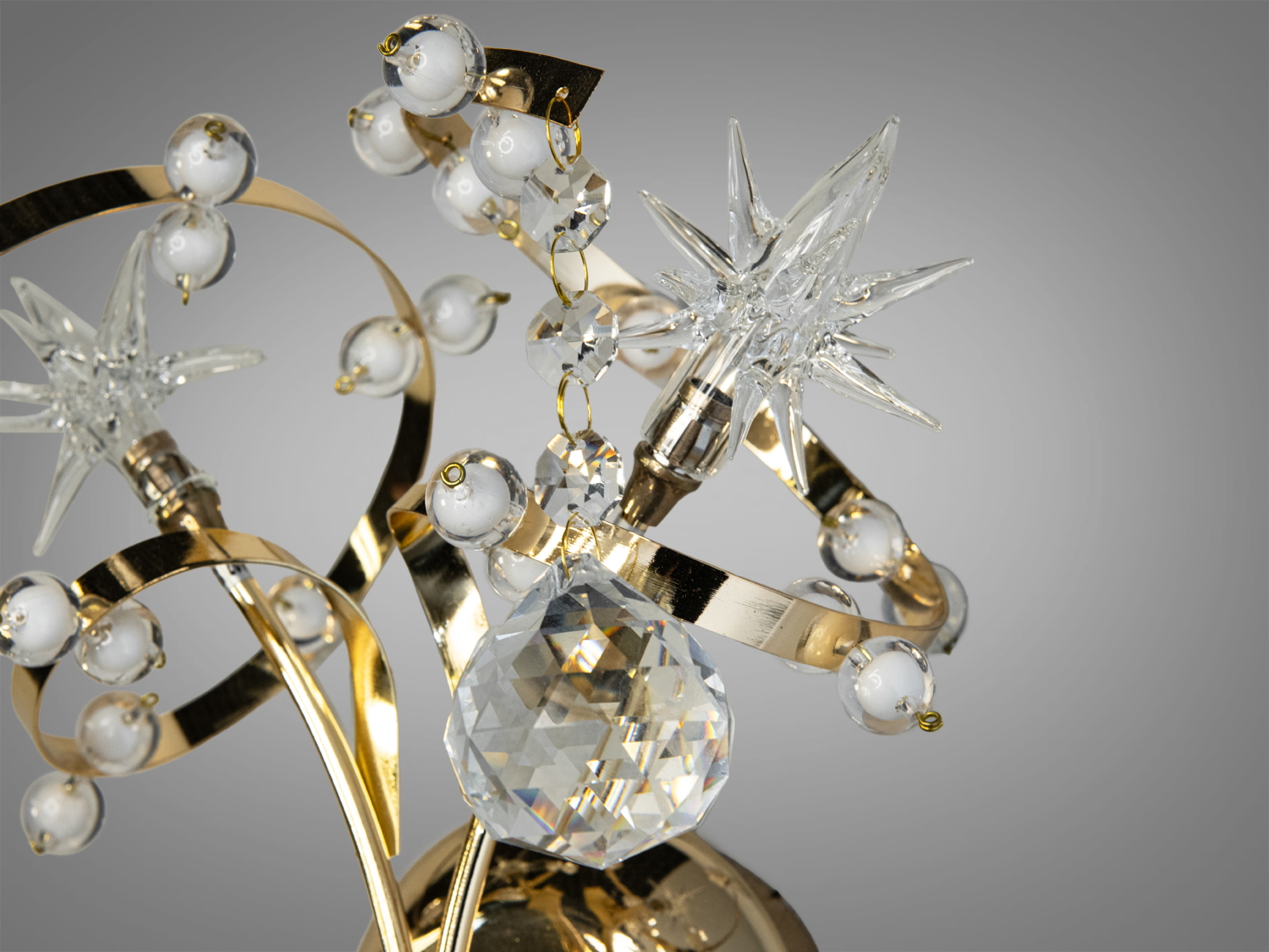 Декоративний елемент світильника у вигляді зірки з прозорого скла, оточений перлами та кришталевими підвісками. Створює ефектний світловий акцент.