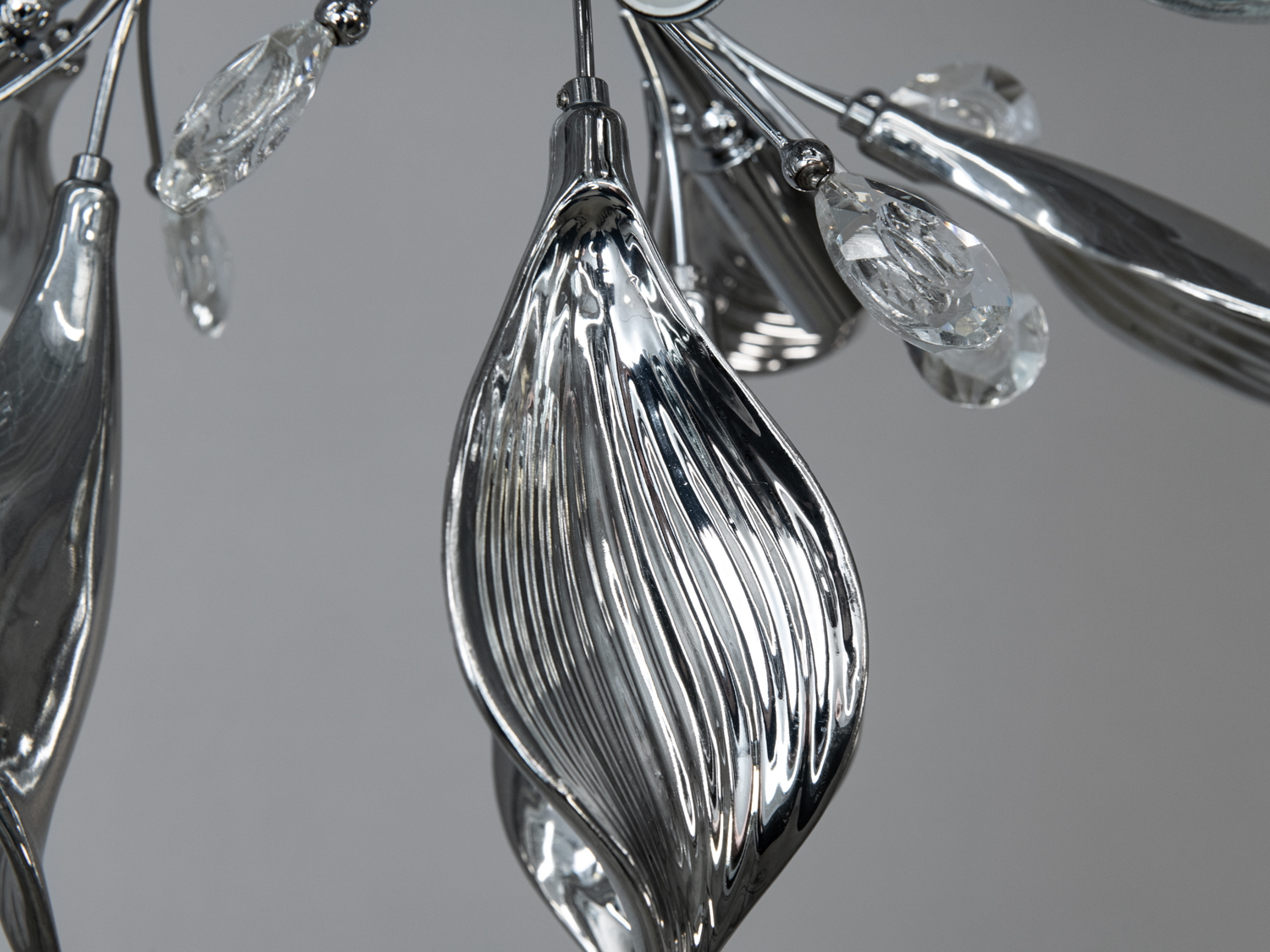 Близький план хромованої люстри з деталями у формі листя та кристалами, які підвішені на тонких стеблах.