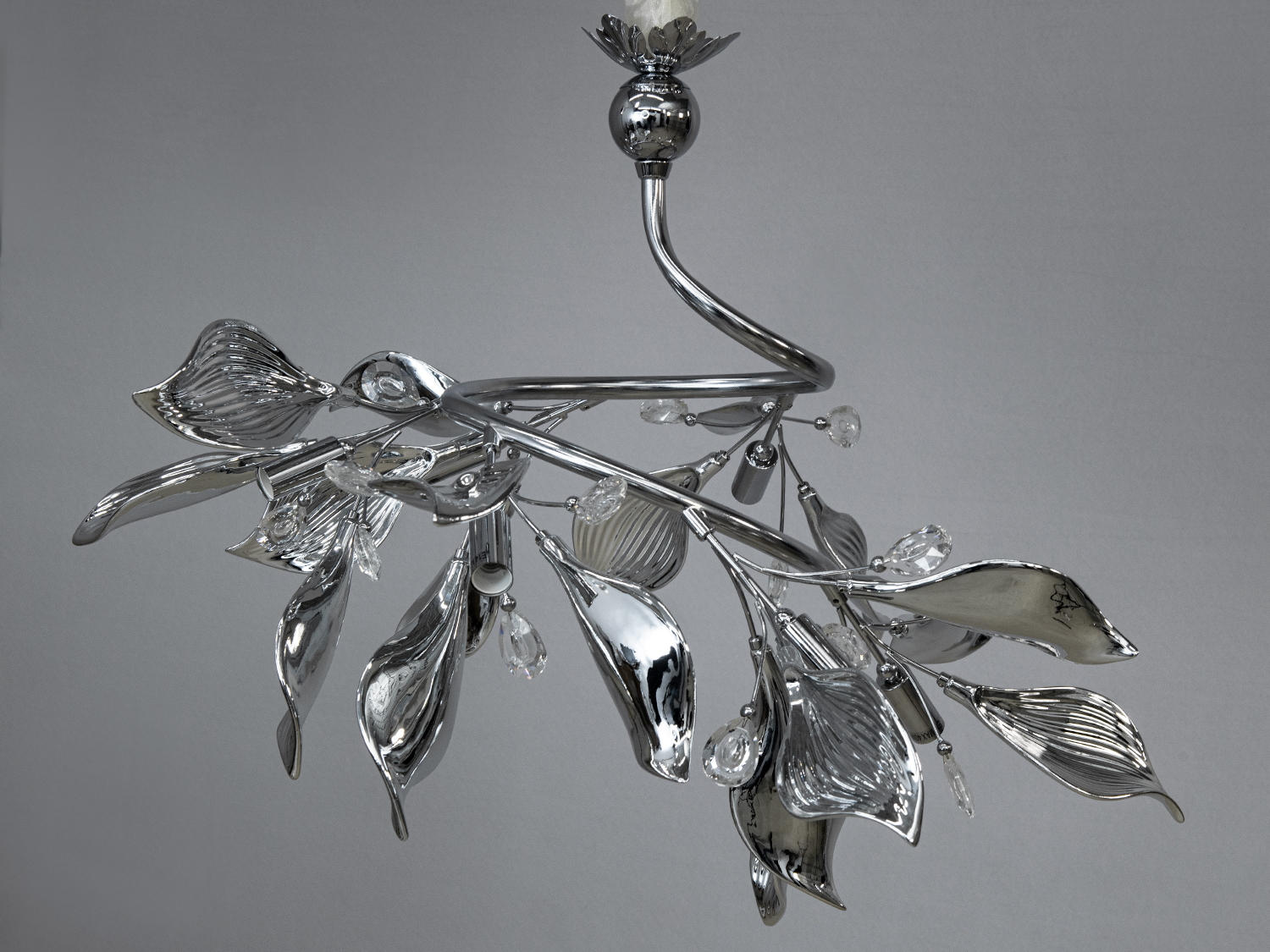 Підвісна люстра з вигнутими металевими листками, прикрашена прозорими кришталевими підвісками, створює відчуття легкості, підходить для спальні.