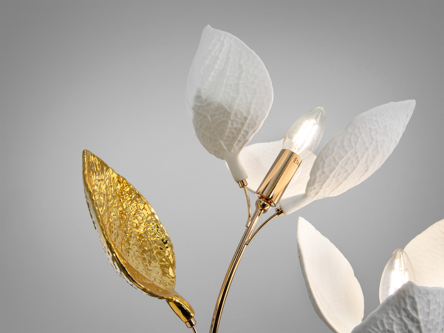 Крупний план лампи з білими та золотими листками, що імітують природний вигляд. Показано деталі текстури та лампочки.