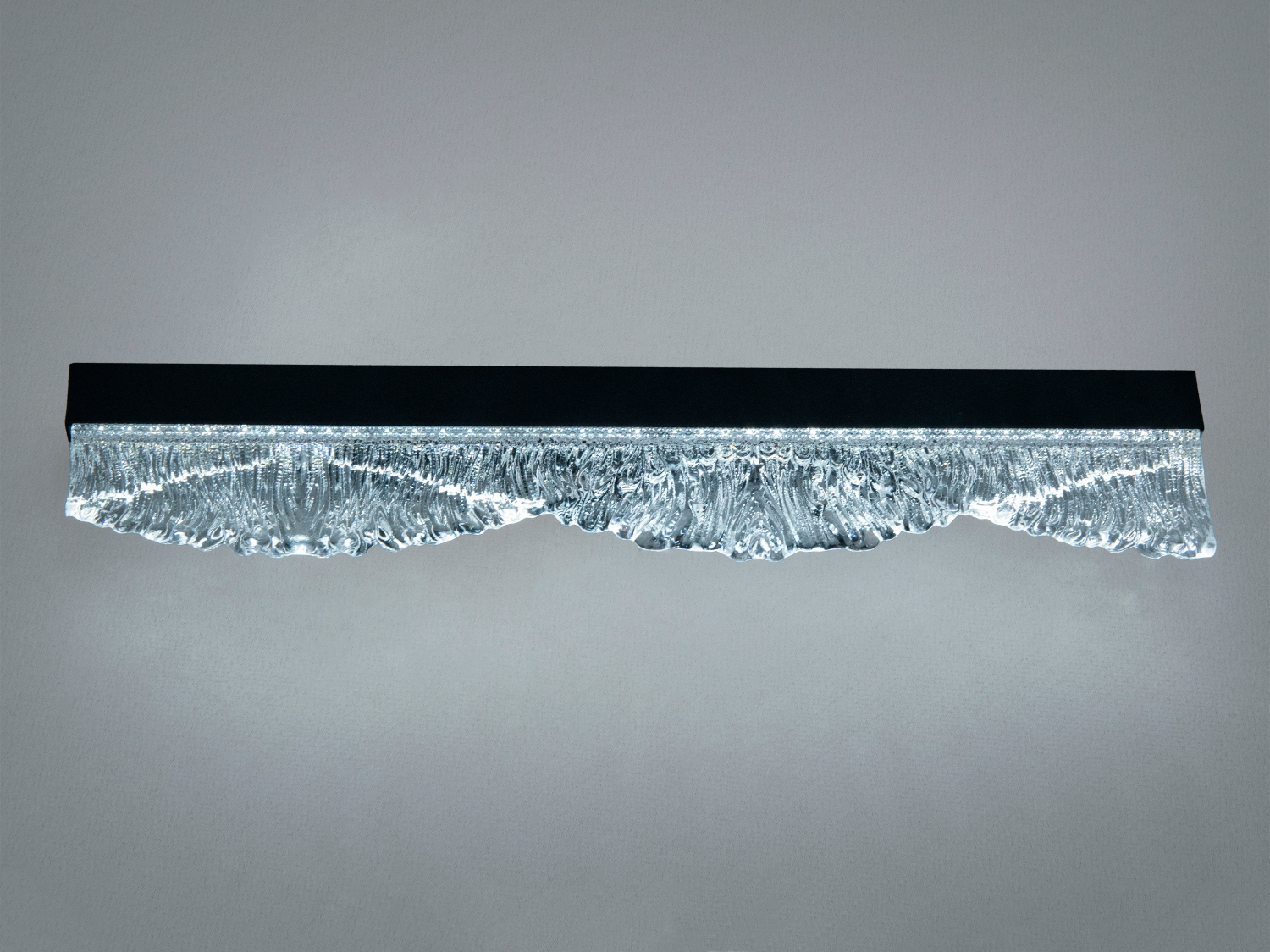 Лінійний світильник з чорним металевим корпусом та рельєфним склом, що створює ефект хвиль. Ідеально для освітлення вітальні.