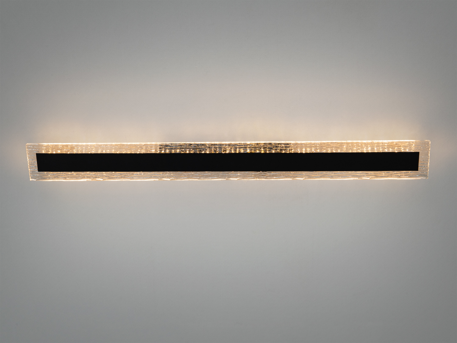 Настінний світильник з прозорого скла з чорною вставкою, що випромінює м′яке світло. Ідеально підходить для сучасного інтер′єру.