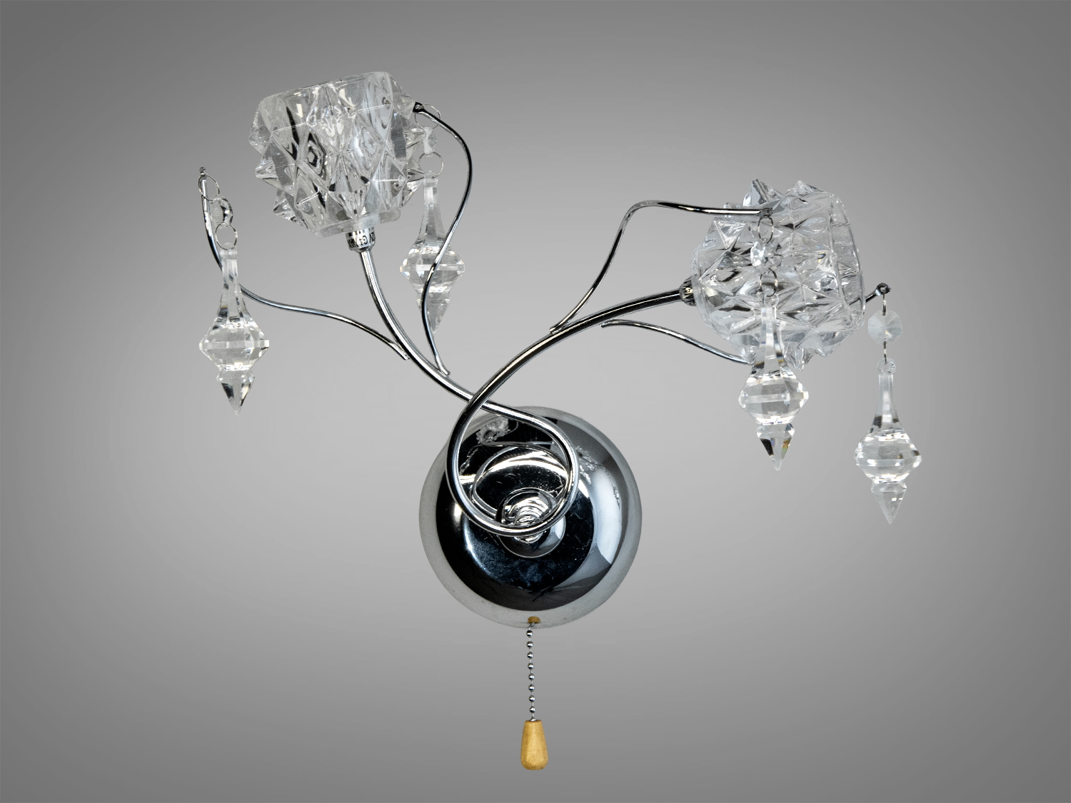 Настінний світильник з кришталевими підвісками, що створюють ефект розсіювання світла. Хромована основа додає сучасного вигляду.