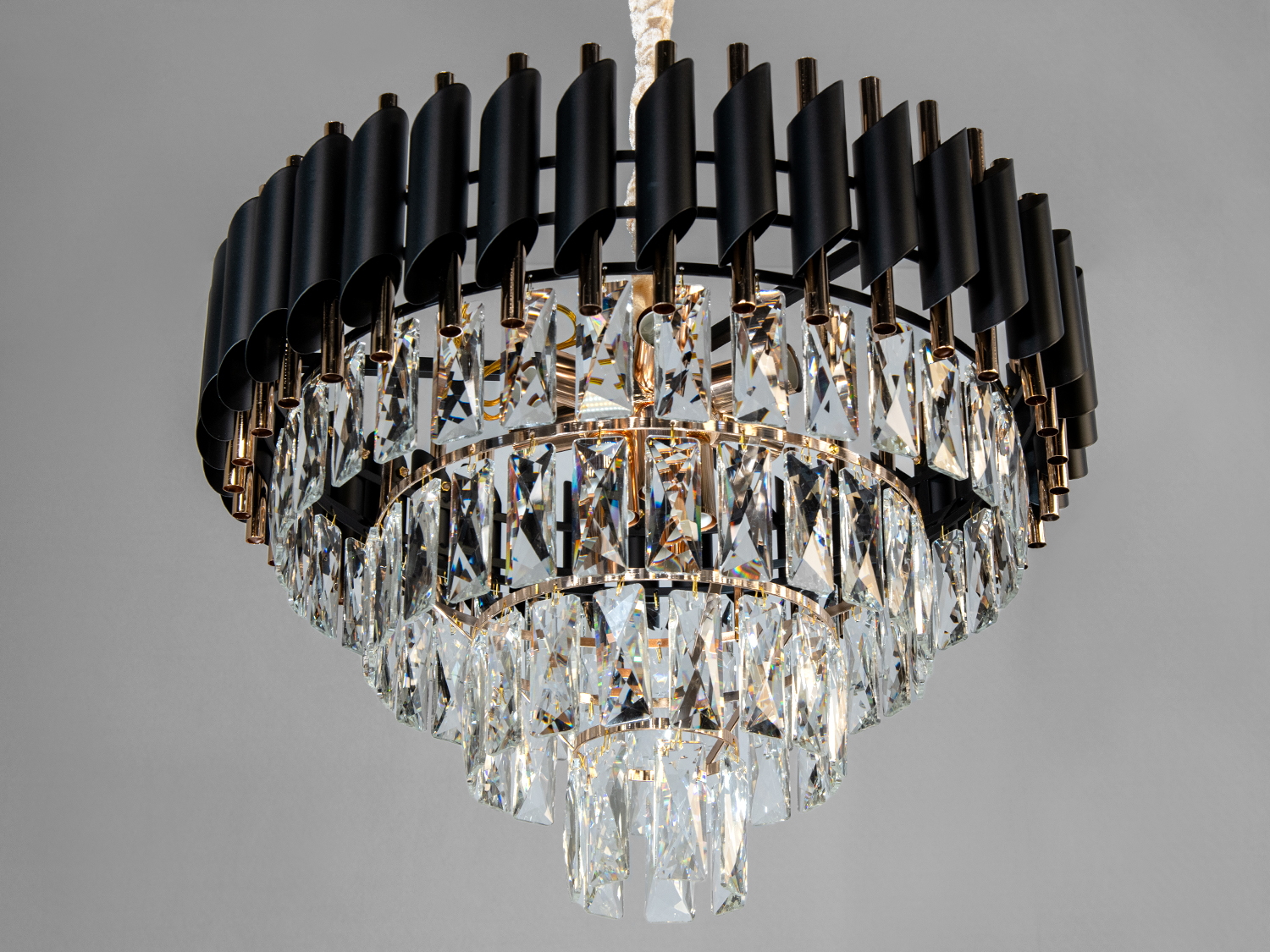 Кругла люстра з кришталевими підвісками, чорним каркасом і золотими деталями, створює елегантний акцент в інтер′єрі.