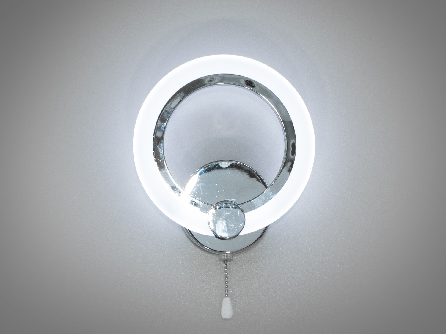 Настінний світильник з круглим LED кільцем і хромованою основою, оснащений шнуровим вимикачем, підходить для сучасного інтер′єру.