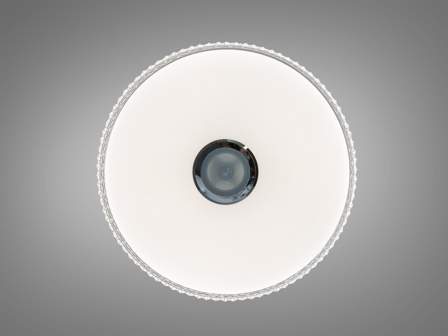 Вид знизу на круглу стельову лампу з центральним динаміком. Гладка поверхня з мерехтливими елементами.