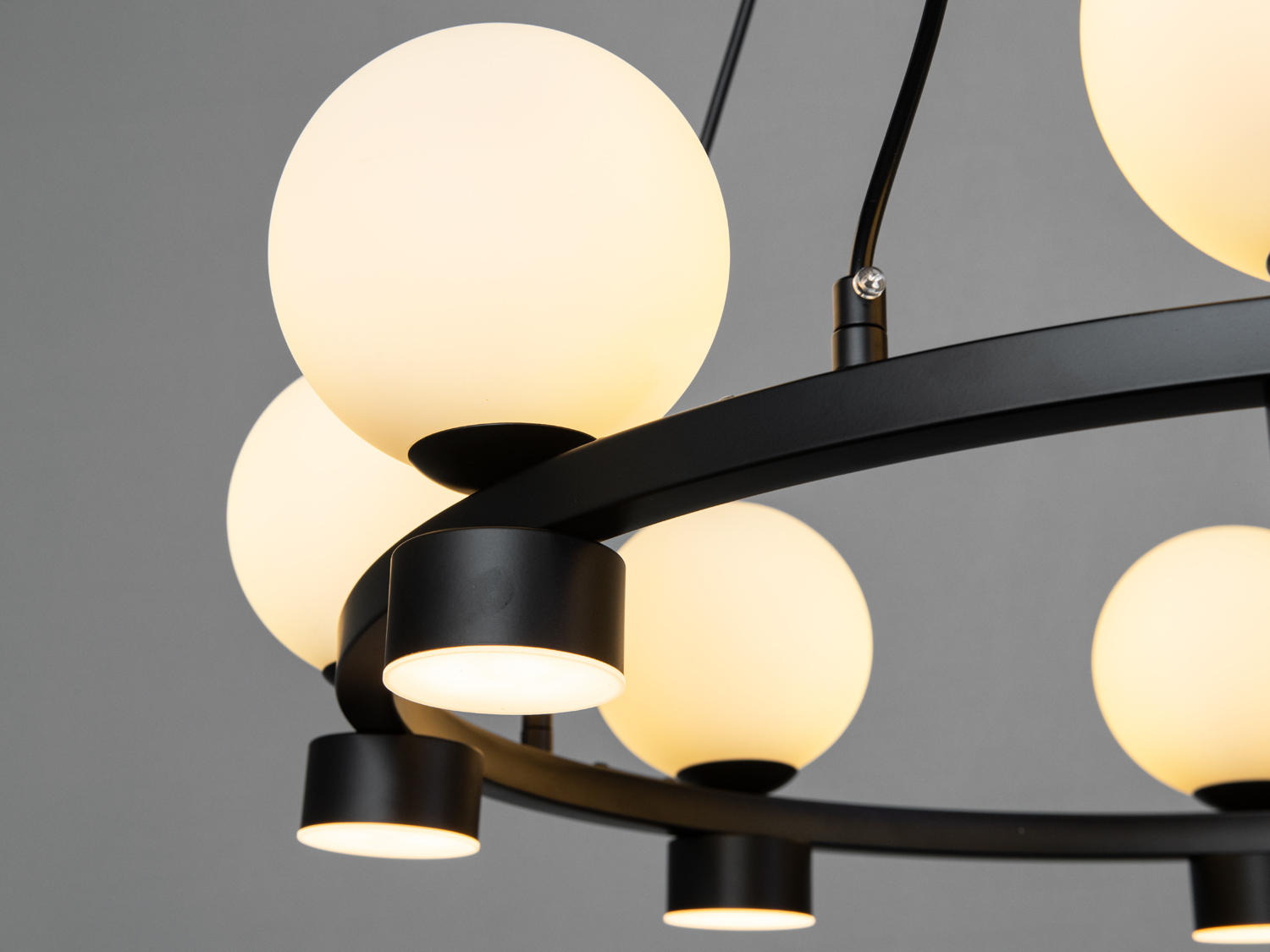 Деталь люстри з матовими кулями, що випромінюють тепле світло. Чорний металевий обідок додає елегантності.