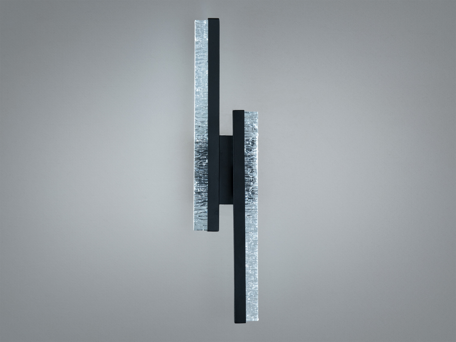 Вертикальний настінний світильник з чорного металу, оснащений акриловими світловими елементами, забезпечує рівномірне освітлення.