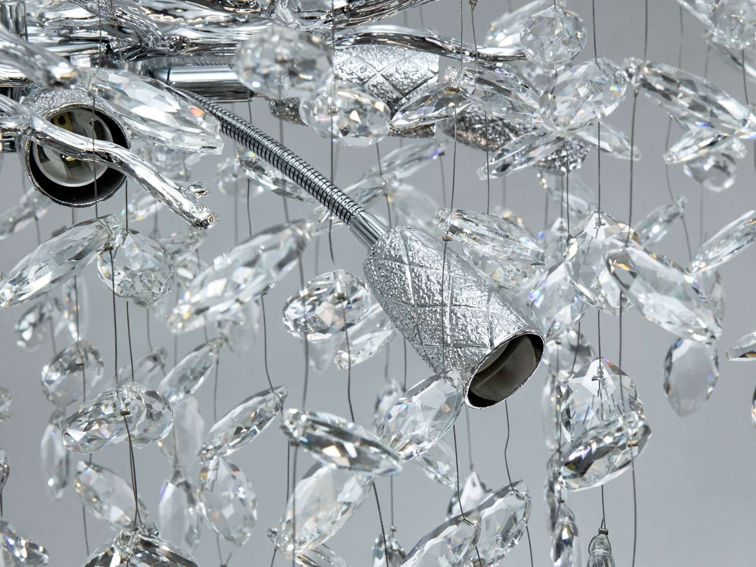 Деталь люстри з кришталевими підвісками, що підкреслює текстуру металевих елементів. Підходить для елегантного освітлення.