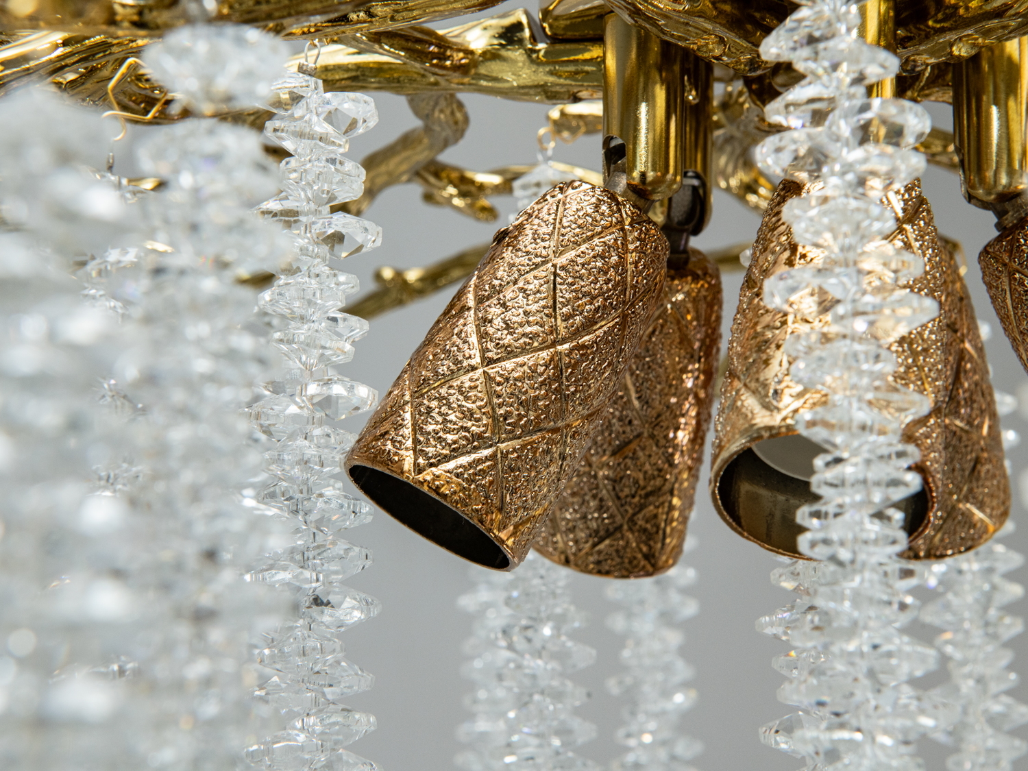 Деталь золотистої люстри з текстурованими металевими елементами та кришталевими підвісками, що підкреслюють розкішний стиль.