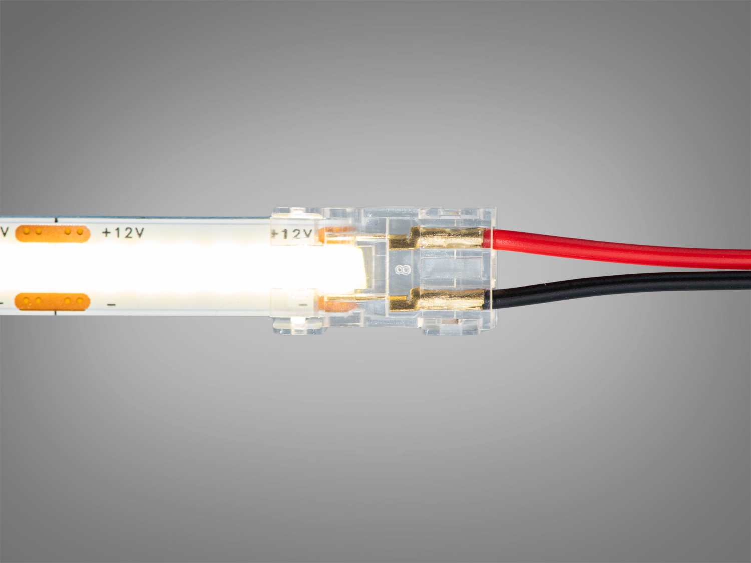 Прозорий конектор з підключеною LED стрічкою, що випромінює біле світло, з червоним і чорним проводами для електричного з′єднання.