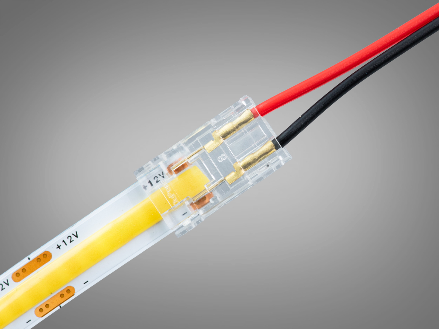 Прозорий конектор з підключеною LED стрічкою, що випромінює жовте світло, з червоним і чорним проводами для з′єднання.
