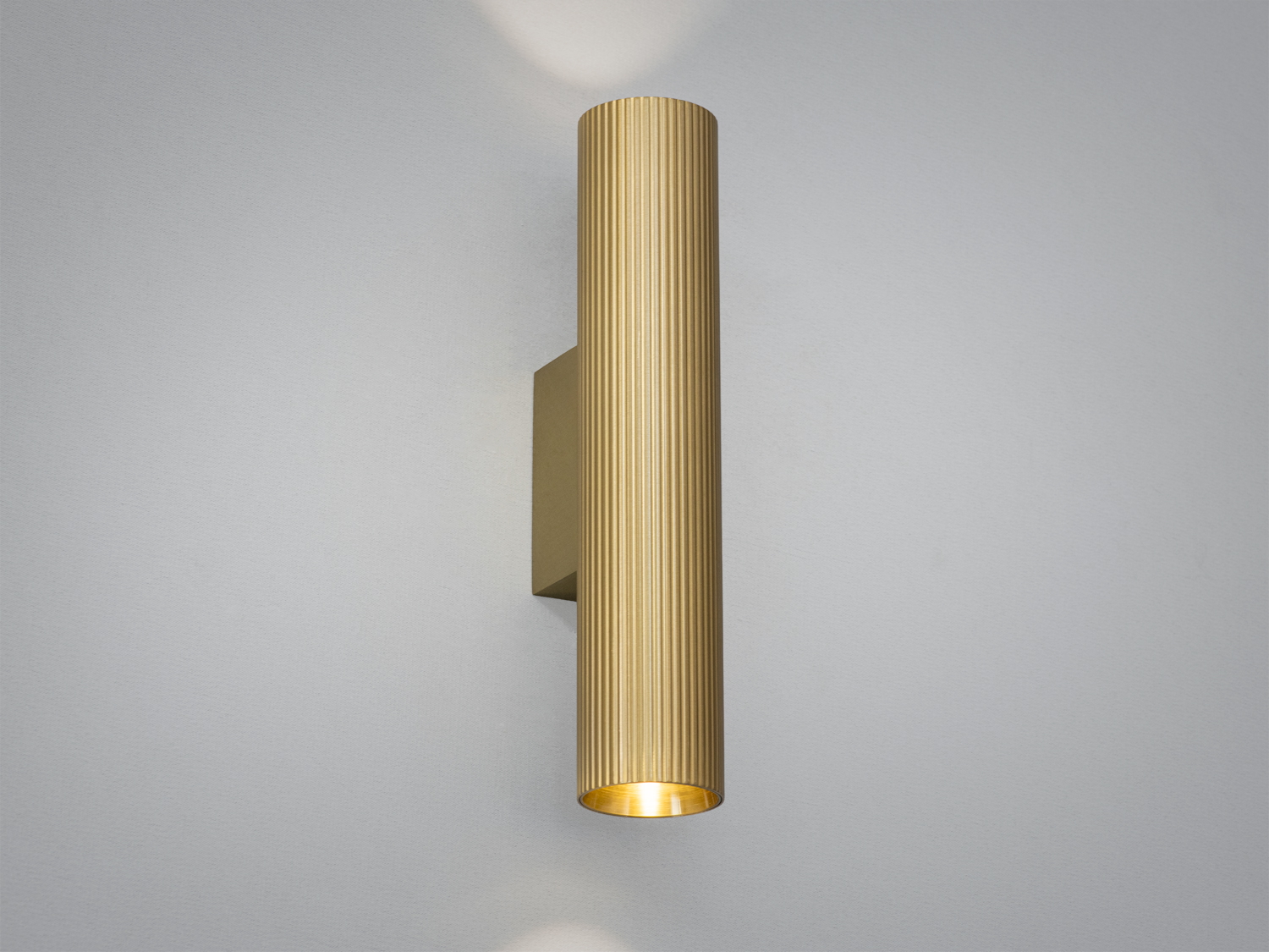 Настінний світильник циліндричної форми, виготовлений з металу, з рифленою текстурою. Підходить для сучасного інтер′єру.