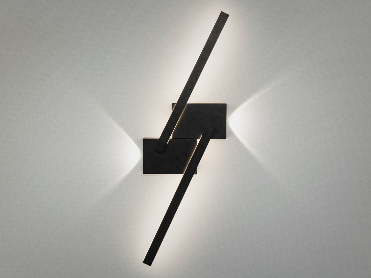 Настінний світильник з чорного металу, що має дві перехресні планки. Випромінює м′яке біле світло, підходить для сучасного інтер′єру.