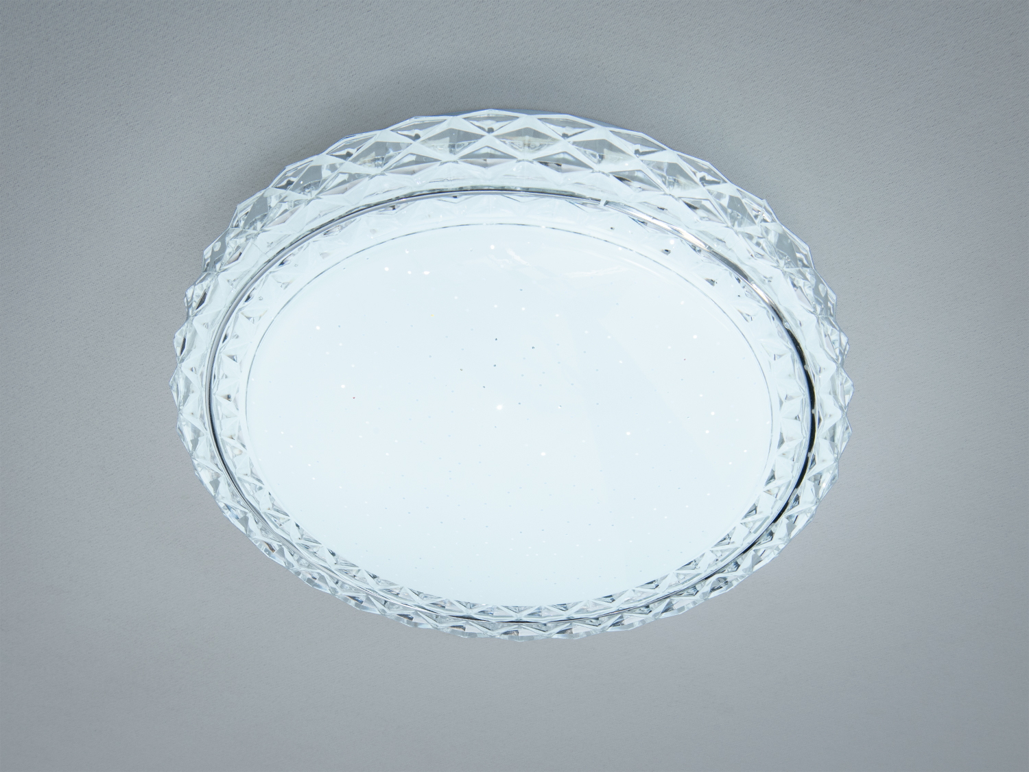 Круглий стельовий світильник з прозорим візерунковим обідком, що створює ефект м′якого розсіювання світла в сучасному інтер′єрі.