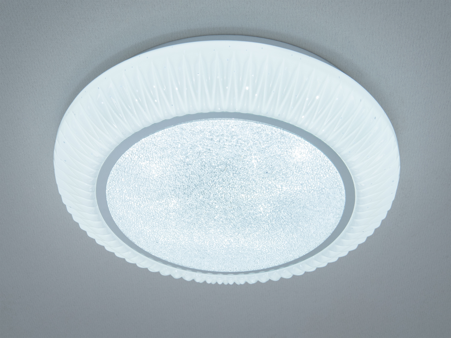 Кругла стельова лампа з текстурованим скляним абажуром і білим пластиковим обрамленням, призначена для загального освітлення приміщення.