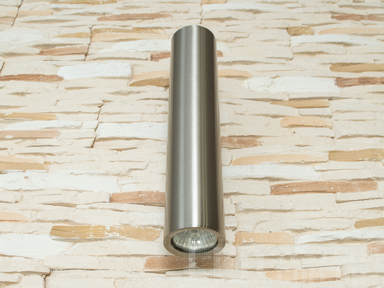 Металевий світильник циліндричної форми, встановлений на стіні з кам′яною текстурою, підходить для акцентного освітлення.